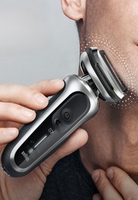 Rasoir électrique avec tête en acier inoxydable, finition argent mat et prise texturée noire, équipé d'un bouton d'alimentation et d'indicateurs LED, incliné pour une utilisation optimale.