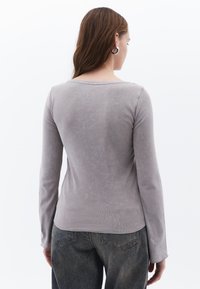 Top aderente a maniche lunghe in morbido tessuto grigio chiaro con scollatura a barco e spalle senza cuciture, abbinato a jeans in denim a vita alta.
