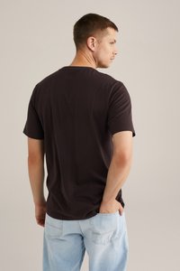 Donkerbruin T-shirt met korte mouwen, ronde hals, zachte katoenstof, losse fitting, gedragen met lichtblauwe baggy jeans, eenvoudig ontwerp, minimale details.
