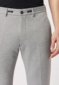Grijze joggingbroek met een gladde textuur, elastische tailleband met trekkoorden, zijnaad en een knoopsluiting.
