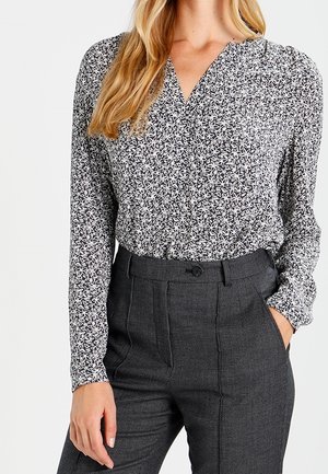 Langärmlige Bluse mit schwarzem und weißem Blumenmuster, ausgestattet mit V-Ausschnitt und legerer Passform, kombiniert mit hoch taillierter grauer Strukturhose.