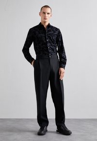 Camicia nera con motivi astratti, maniche lunghe, chiusura con bottoni; abbinata a pantaloni neri a vita alta e sneakers nere con lacci.