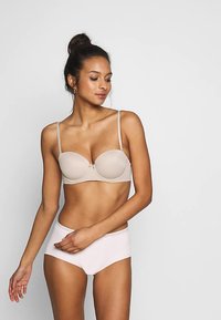 Reggiseno imbottito beige con spalline regolabili e piccolo fiocco decorativo; abbinato a slip a vita alta rosa chiaro, tessuto liscio.