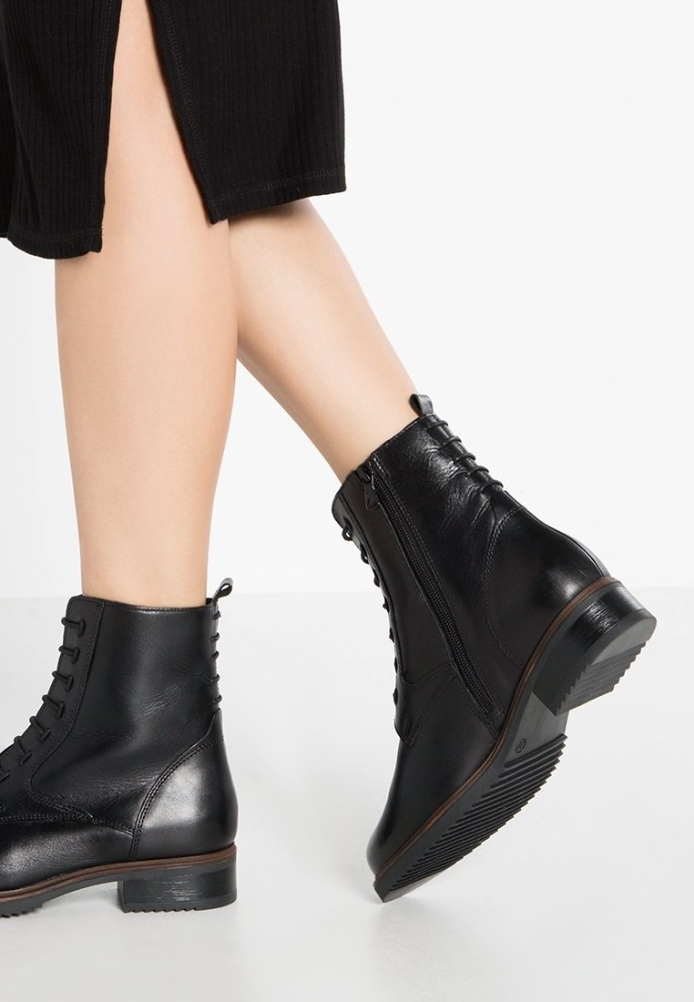 Bottes basses en cuir noir avec bout rond, laçage à l'avant, fermeture éclair latérale et semelle texturée. Présentent des coutures et une finition lisse.