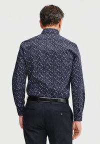 Granatowa koszula z długim rękawem i klasycznym kołnierzykiem, ozdobiona wielokolorowym wzorem kwiatowym, zestawiona z ciemnymi spodniami i czarnym paskiem.