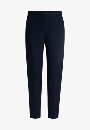Pantaloni sartoriali blu navy con un tessuto liscio, vestibilità slim e dettagli con piega. Presentano una vita piatta e nessun fissaggio visibile.