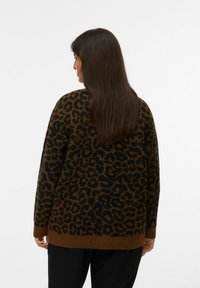 Pull en tricot à imprimé léopard marron et noir, coupe décontractée, manches longues, poignets et ourlet côtelés, texture douce, porté sur un pantalon noir.