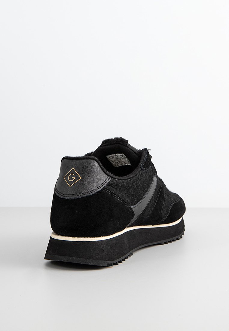 Zapatilla negra con parte superior de ante y acentos texturizados, con una entresuela blanca en contraste y detalle del logo en el talón.
