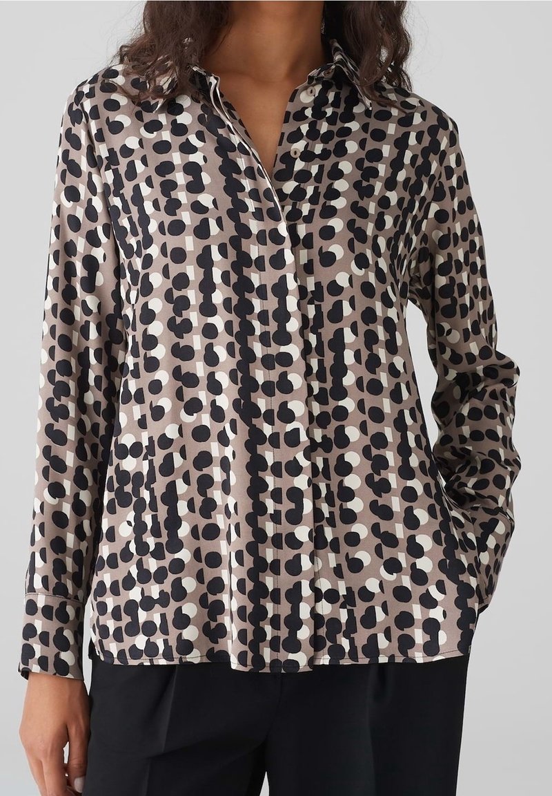 Button-up blouse in silky fabric. Features a beige background with black and white circular patterns. Long sleeves and collar detail.