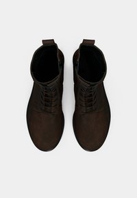 Bottes de cheville en cuir marron avec une texture lisse, bout rond, laçage à l'avant et languette à l'arrière. La semelle est plate et noire.