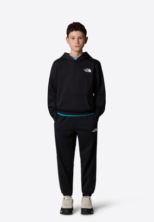 Sudadera negra con bolsillo frontal y logo en el pecho, combinada con pantalones de chándal a juego que tienen una cintura azul y zapatillas de senderismo grises.