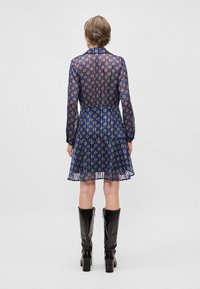 Jūros jėgos skaidrus suknelė su auksiniais apvaliais raštais, ilgomis rankovėmis ir sluoksniuota sijonė. Derinama su juodomis aukštakulnėmis batais iki kelių.