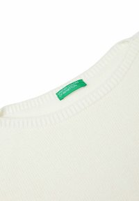 Maglione bianco a coste con scollo rotondo. Presenta un'etichetta verde con la scritta "UNITED COLORS OF BENETTON" sul collo. Texture morbida.