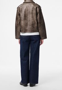 Braune Lederjacke im Crop-Design mit glatter Textur und weiten Ärmeln, kombiniert mit dunkelblauen, weit geschnittenen Jeans. Rückansicht.