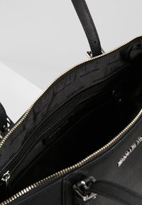 Sac à main en cuir noir ouvert avec fermeture éclair dorée, montrant la doublure intérieure et une poche zippée à l'intérieur.