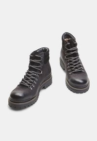 Botas de senderismo de cuero negro con suelas de goma resistentes, ojales de metal y cordones grises. Presentan un cuello acolchado para mayor comodidad.