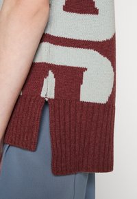 Sweter wykonany na drutach, w jasnoszarym kolorze z kontrastowym bordowym wzorem graficznym, z prążkowanym dołem i bocznymi rozporkami zapewniającymi wentylację.