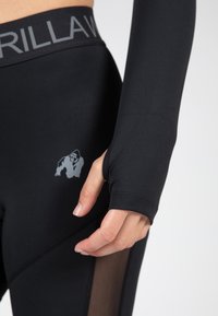 Zwarte sportleggings met meshedetails en een logoprint. De stof is glad en aansluitend, met een hoge tailleband en duimhulsen op de mouwen.