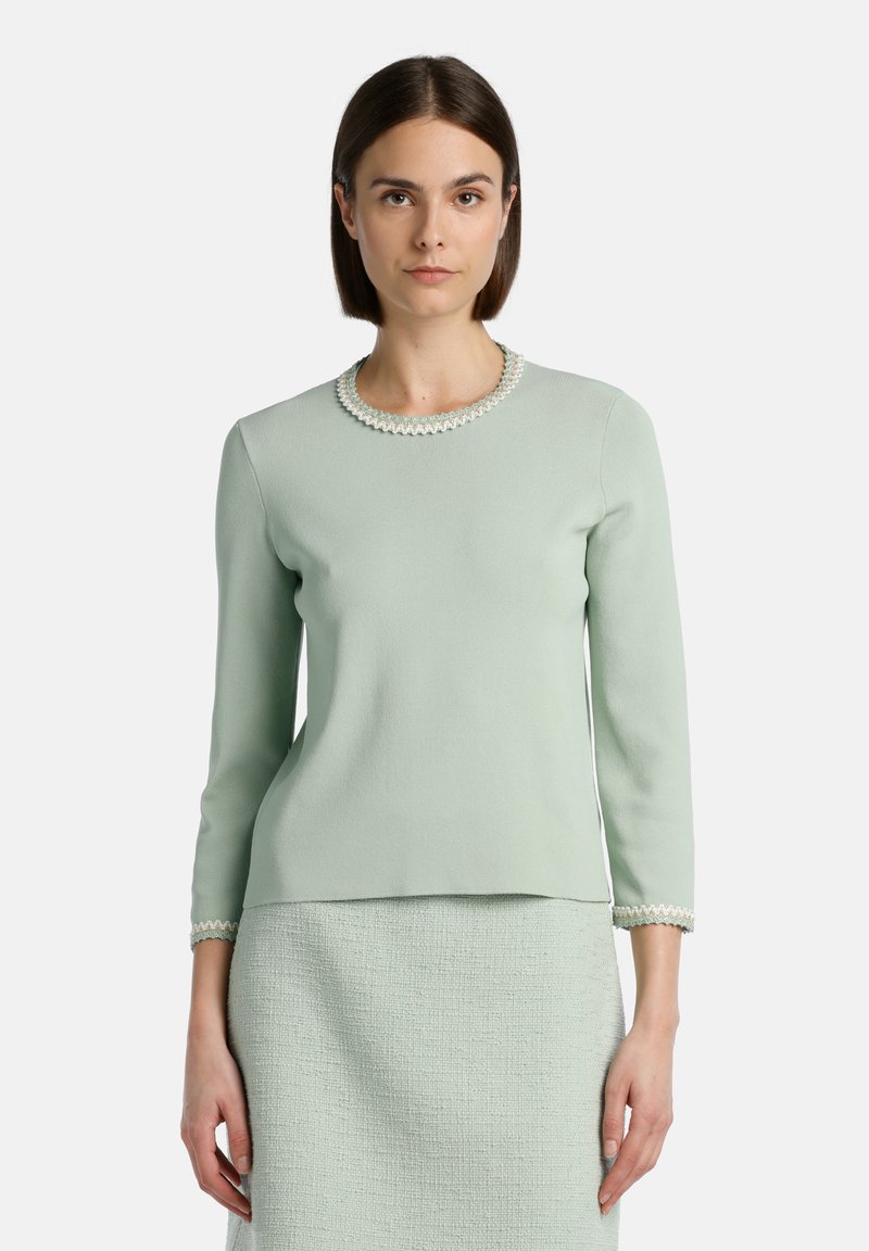Top verde cu mânecă lungă, cu textură ribbed și margine decorative cu volane la gât și la manșete. Asortat cu o fustă texturată care se potrivește.