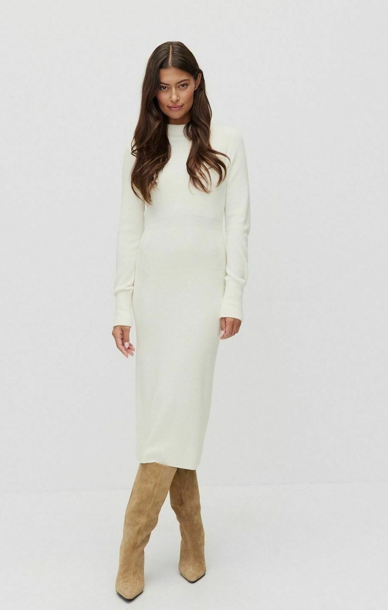 Robe tricotée crème longue et ajustée avec des manches longues, associée à des bottes en daim tan jusqu'au genou. Design simple, sans motifs ni accessoires visibles.