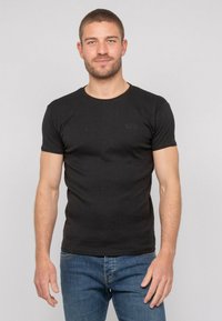 T-shirt noir à manches courtes en coton, avec un col rond et un logo discret sur la poitrine, associé à un jean en denim bleu.