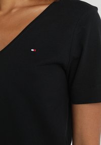 Schwarzes Baumwoll-T-Shirt mit V-Ausschnitt. Verfügt über ein kleines, gesticktes Logo in Rot, Weiß und Blau auf der linken Brustseite. Kurze Ärmel.