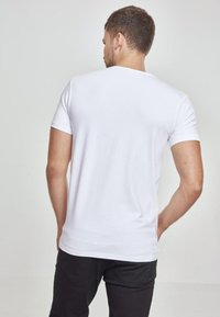 Tricou scurt cu mâneci din bumbac fin, de culoare albă, cu un decolteu clasic și un design ajustat, purtat cu pantaloni închiși la culoare.