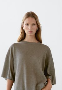 Lekki, oversize oliwkowy sweter z krótkimi rękawami i okrągłym dekoltem. Miękka faktura i luźny krój, idealny na codzienne noszenie.
