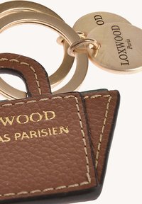 Porte-clés en cuir marron avec une surface texturée, des anneaux métalliques dorés et un texte doré en relief "LOXWOOD PARISIEN." Étiquettes rondes dorées attachées.