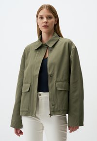 Giacca leggera verde oliva con colletto, chiusura a scatto e due tasche frontali; presenta una vestibilità comoda con spalle leggermente abbassate.