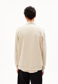 Beiger Pullover-Sweatshirt aus strukturiertem Stoff, mit gerippten Bündchen und einem lässigen Schnitt, das eine weiche, glatte Oberfläche und ein minimalistisches Design bietet.