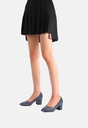 Scarpe con tacco alto blu navy, con punta affusolata e tacco a blocco. Il materiale appare liscio, in abbinamento a una gonna nera plissettata con strisce.