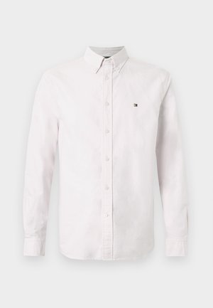 Balta marškinių apykaklė su ilgomis rankovėmis, pagaminta iš medvilnės, su nedideliu logotipu kairėje krūtinės pusėje ir klasikinio tipo apykakle.