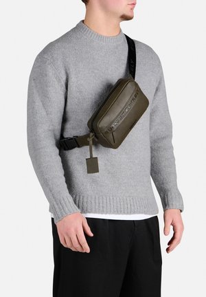 Olivengrøn nylon bæltetaske med prægede logo, lynlåslukning, justerbar sort rem og mærkede detaljer, båret over brystet.