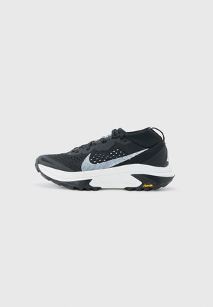 Chaussure de sport noire et blanche avec une semelle texturée, un logo Swoosh réfléchissant et une marque Vibram sur la semelle du talon.