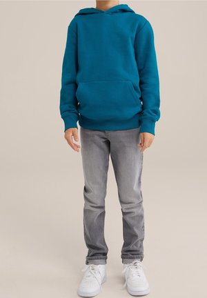 Teal hoodie with a kangaroo pocket, ribbed cuffs, and hem. Paired with gray jeans and white sneakers, standing on a neutral background.
