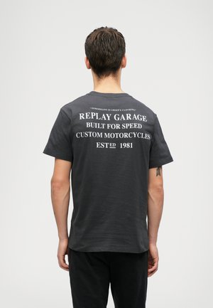 Graues T-Shirt mit kurzen Ärmeln und weißem Grafiktext auf der Rückseite, das den Markennamen und Motorrad-Motive zeigt. Aus Baumwollmaterial, mit lockerer Passform.