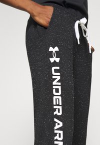 Zwarte joggingsbroeken met een gespoten textuur, voorzien van een elastische tailleband en een witte trekkoord, en een wit logo op het linkerpoot.