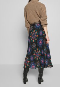 Bruin gebreid sweater gecombineerd met een geplooide zwarte rok met een meerkleurig bloemenpatroon. Zwarte kniehoge laarzen maken de look compleet.