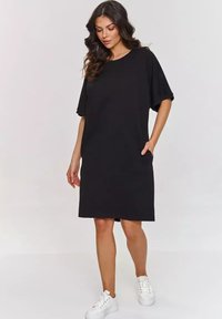 Czarna sukienka krótko rękawowa z okrągłym dekoltem i kieszeniami, wykonana z miękkiego materiału. Noszona z białymi trampkami. Prosty i luźny krój.