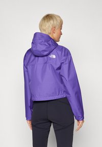 Giacca impermeabile viola con cappuccio, caratterizzata da un design cropped, polsini elasticizzati e un logo sulla schiena. Tessuto morbido e leggero.
