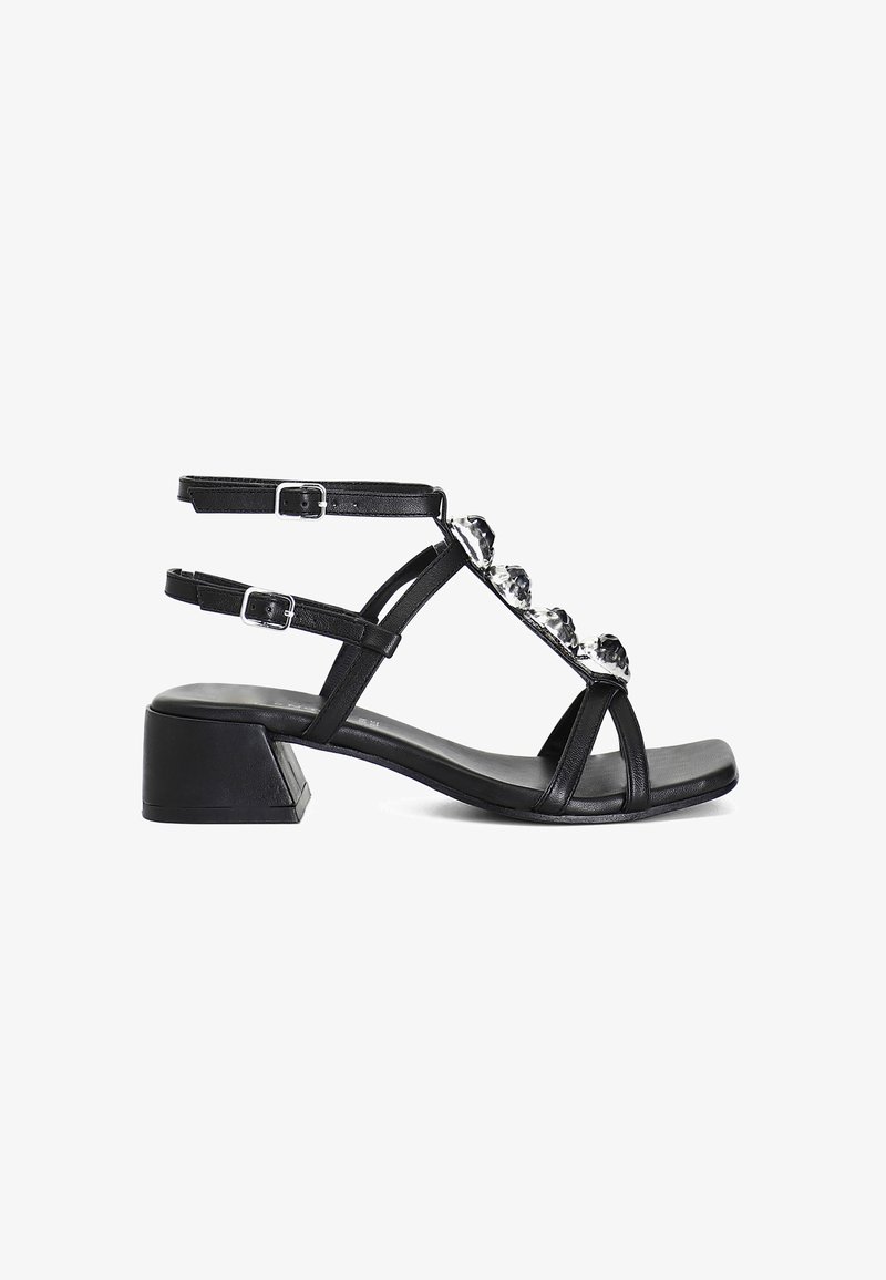 Sandalo in pelle nera con tacco a blocco, dotato di cinturini alla caviglia regolabili e decorazioni in strass sul dorso del piede, con un design minimalista.