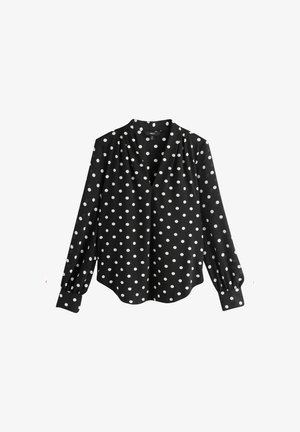 Blouse noire à pois blancs, col en V, manches longues bouffantes avec détails aux poignets, texture de tissu lisse, ourlet incurvé.