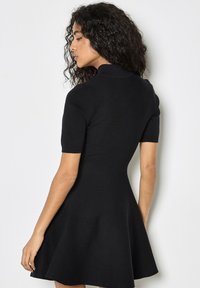 Abito nero a maglia con maniche corte, corpino aderente e gonna svasata. Presenta un collo alto e una texture morbida. Vista laterale mostrata.