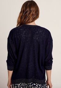 Marineblauwe gebreide trui met een losse pasvorm, driekwart mouwen en een textuurdesign. Metallic accenten bij de mouwen en de zoom.