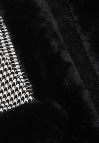 Sort faux fur stofkanter rammer et tekstureret houndstooth-mønster i sort og hvid. Materialerne kontrasterer i blødhed og visuel detalje.