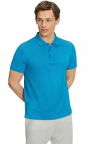 Polo shirt turchese a maniche corte realizzato in tessuto traspirante, con colletto e patta a tre bottoni. Abbinato a pantaloni sportivi grigi.