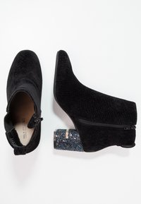 Bottines noires en daim avec un motif texturé, fermeture éclair, et un talon bloc pailleté avec des accents irisés.