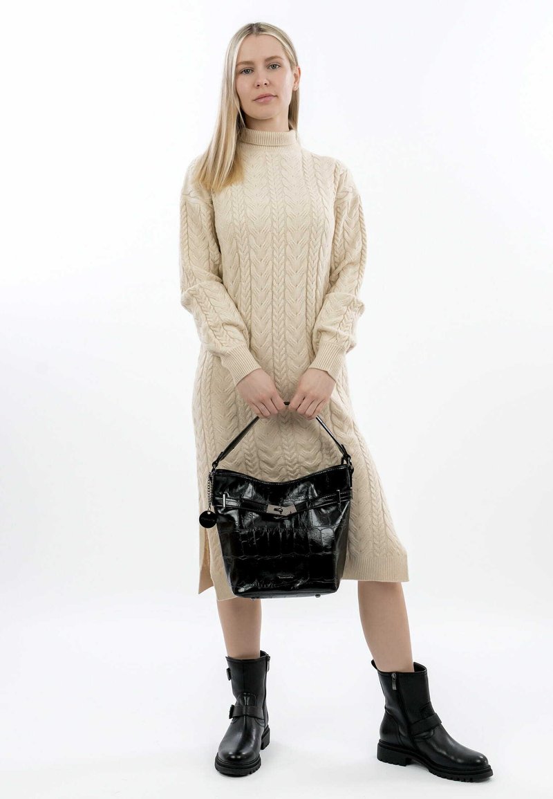 Abito maglione in maglia a treccia beige con maniche lunghe, abbinato a una borsa nera lucida in ecopelle coccodrillo e stivaletti neri alla caviglia.