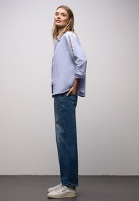 Lyseblå skjorte med knapper og stribede ærmer, kombineret med blå jeans med lige ben og hvide sneakers. Simpelt design med en afslappet pasform.